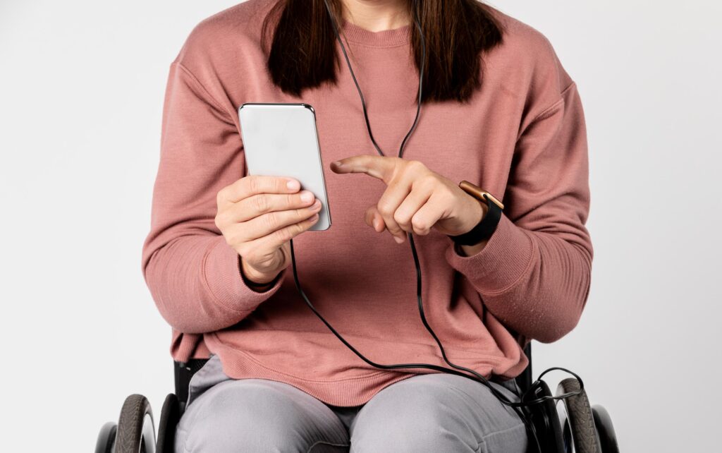 Person i kørestol som bruger en mobiltelefon med høretelefoner i ørerne.